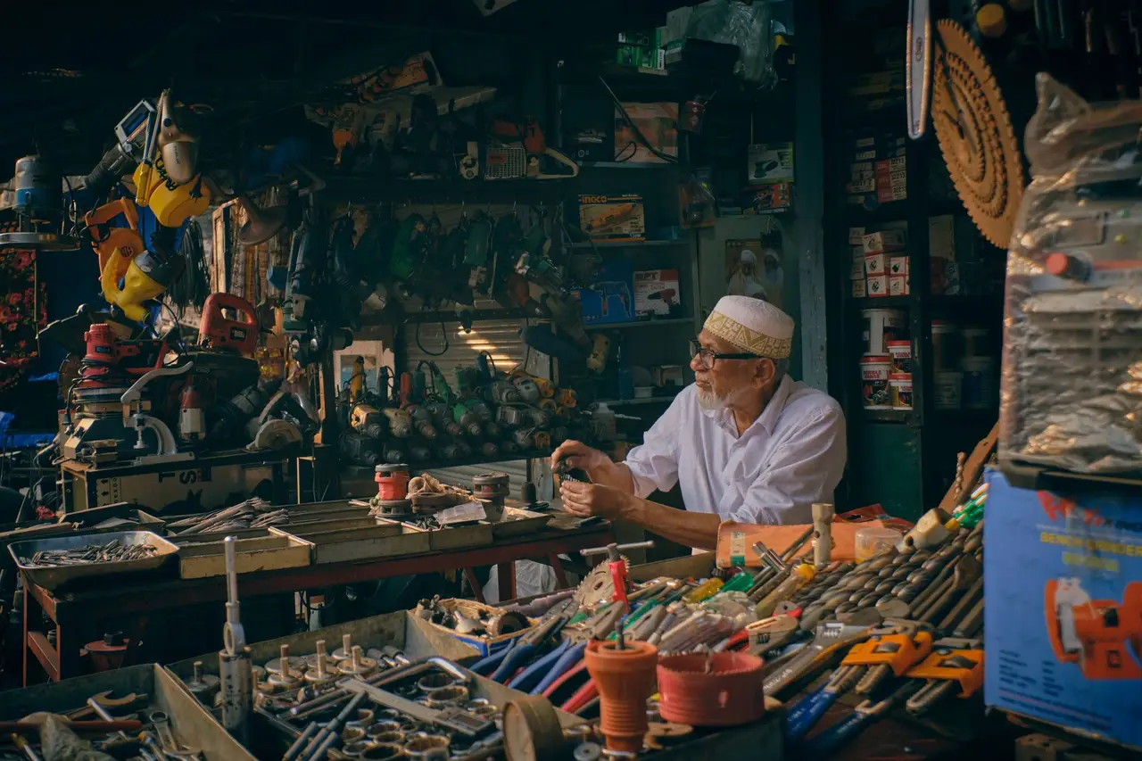 A shopkeeper at a counter surrounded by thousands of tools and parts